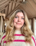 Woman with blonde hair wearing a white sweater with pink stripes indoors.
